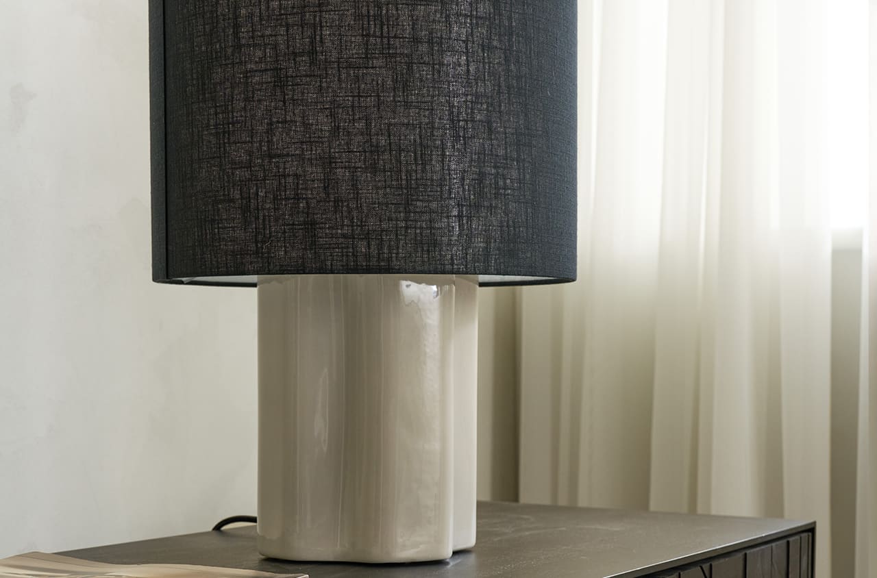 Tischleuchte mit dunklem Schirm und hellem Fuß, die für eine ruhige, warme Stimmung sorgt.